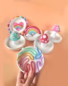 a hand is holding an assortment of colorful plastic toys on a pink surface with mushrooms, rainbows and mushroom tops