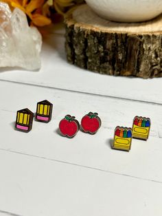 three pairs of colorful earrings sitting on top of a white table next to an orange flower