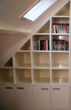 an attic bedroom with white bookcases and skylight above the bookshelves