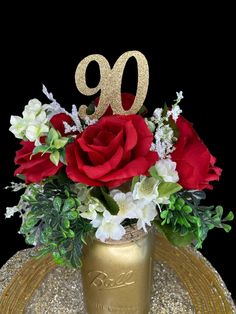 a gold vase filled with red roses and white flowers on top of a table next to a golden plate