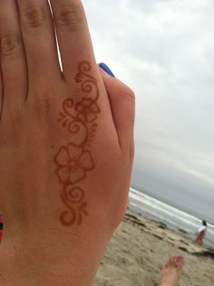 a person's hand on the beach with a henna painted on their palm