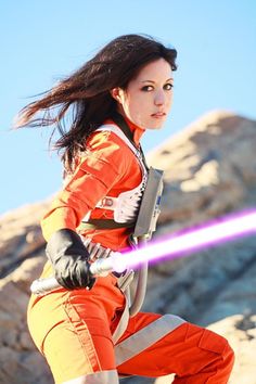 a woman in an orange outfit holding a purple light saber