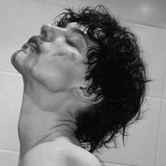 black and white photograph of a man with wet hair in a bathtub looking up