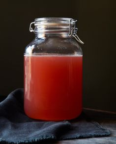 a glass jar filled with liquid sitting on top of a wooden table next to a blue cloth