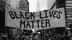 a banner that says black lives matter in the middle of a city with tall buildings