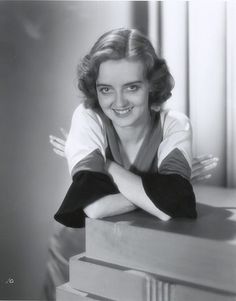 black and white photograph of a woman leaning on top of a dresser with her arms crossed