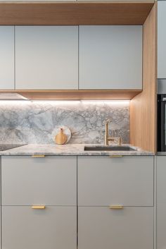 a kitchen with white cabinets and marble counter tops, gold pulls on the cupboards