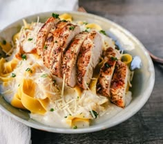 a white plate topped with pasta and sliced chicken breast on top of cheese covered noodles