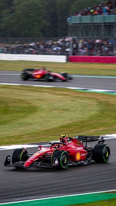 a red race car driving on a track with people watching from the sidelines behind it