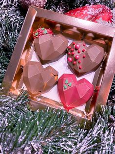 three heart shaped chocolates in a box on a christmas tree with ornaments around them