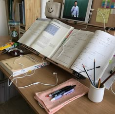 an open book sitting on top of a wooden desk next to a cup with pencils