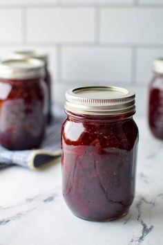 three jars filled with raspberry jam sitting on a counter top next to a spoon