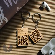 a wooden keychain with a qr code on it next to ear buds