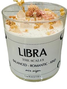 a candle with flowers in it sitting on top of a white table next to a sign that reads libra the scales balanced romantic kind