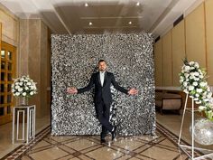 a man in a tuxedo standing next to a wall with flowers on it