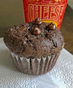 a chocolate muffin sitting on top of a white napkin next to a bag of cheese