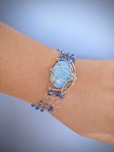 a woman's arm wearing a bracelet with a blue glass bead and wire design