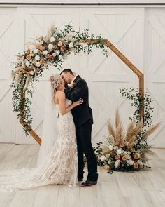 a bride and groom kissing in front of an arch decorated with greenery and flowers