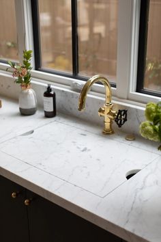 a kitchen sink with a gold faucet and marble counter top next to a window