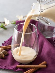 a pitcher pouring milk into a glass filled with almonds and cinnamon on a purple cloth