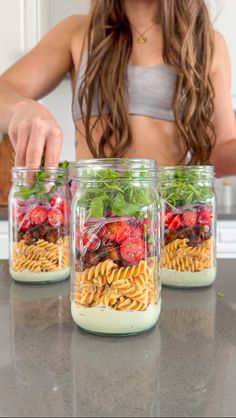 a woman is making pasta salad in mason jars