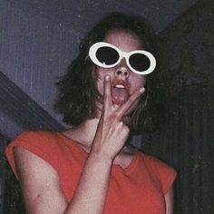 a woman in red shirt holding up her hands to her face while wearing large white sunglasses