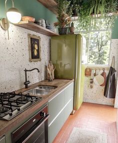 a small kitchen with green walls and white cabinets is pictured in this image, there are plants growing on the shelves above the sink