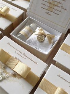 many white boxes with gold ribbons and bows on them, all containing wedding rings or brooches