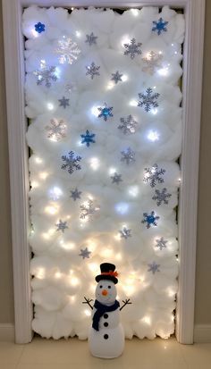 a snowman is standing in front of a white wall decorated with balloons and lights