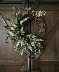 a wreath hanging on the side of a barn door with greenery and leaves attached to it