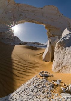 the sun is shining through an arch in the desert