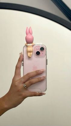 a person holding an iphone case with a small doll on it's back in front of a car