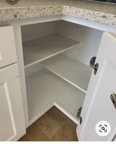 an open cabinet in a kitchen with marble counter tops