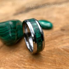 two wedding bands with green marble inlays are on top of a wooden table