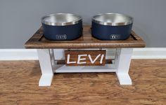 two metal bowls sitting on top of a wooden stand with the word levi written below them