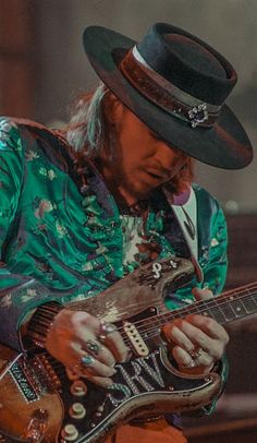 a man with long hair wearing a hat and playing an electric guitar in front of a microphone