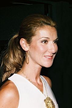 a woman in a white dress with gold jewelry on her neck and hair pulled back