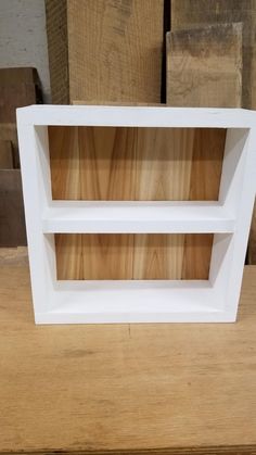 two white shelves sitting on top of a wooden table next to stacks of wood planks