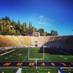 an empty football stadium with people on the field and trees in the backgroud