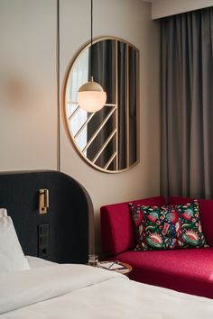 a red couch sitting next to a bed in a bedroom under a round mirror on the wall