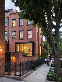 two people walking down the sidewalk in front of a brick building with many windows on it