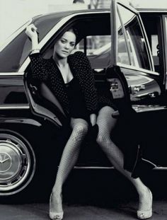 a woman sitting on the door of a car with her legs crossed and wearing fishnet stockings