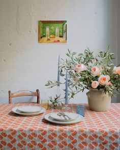 the table is set for two with plates and flowers in vases next to it