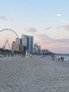 people are walking on the beach with ferris wheel in the foreground and tall buildings in the background