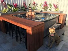 a dog sitting in front of a hot tub on top of a wooden table next to two stools