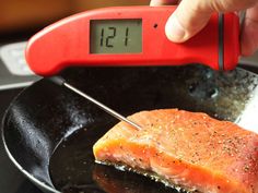 a person using a thermometer to check on a piece of fish in a frying pan