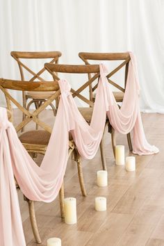 the chairs are lined up with pink draping and candles in front of them