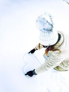 a woman kneeling down in the snow with a hat on her head and mittens