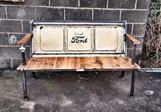 an old metal and wood bench sitting in front of a brick wall with the word ford painted on it