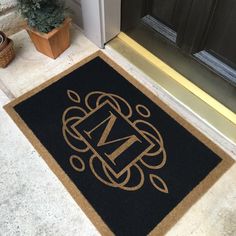 a door mat with the letter m on it in front of a door and potted plant